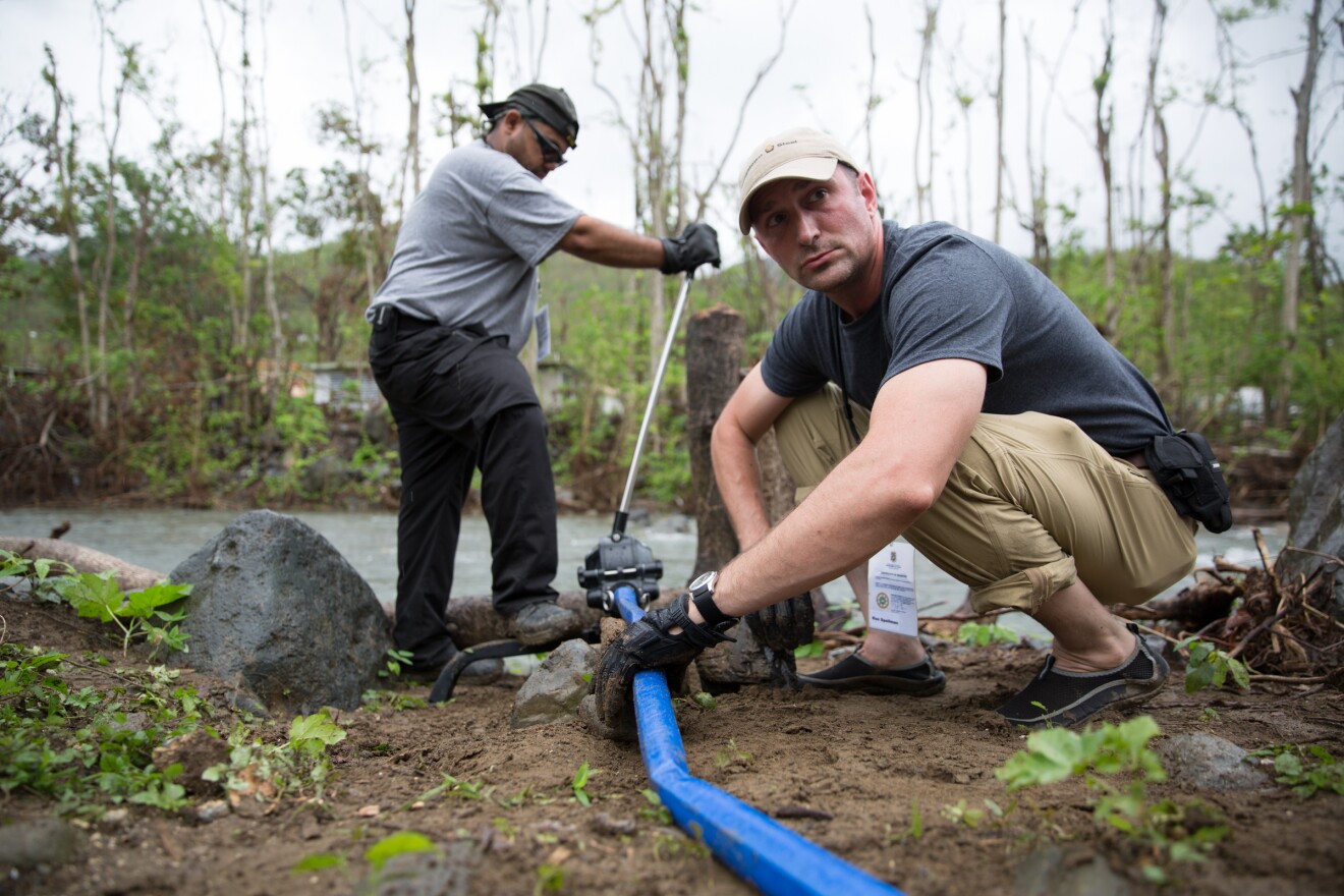 Ron Spellman of Canton, Connecticut -- who's served in the U.S. Coast Guard and now is in the Air Force Reserves, sets up a hose to pump water from the river to the purifying tank. U.S. Army veteran Pablo Soto works the pump in the background.